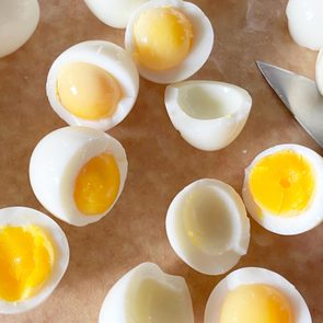 Boiled eggs are sliced open, revealing various yolk consistencies, on a cutting board next to a knife.