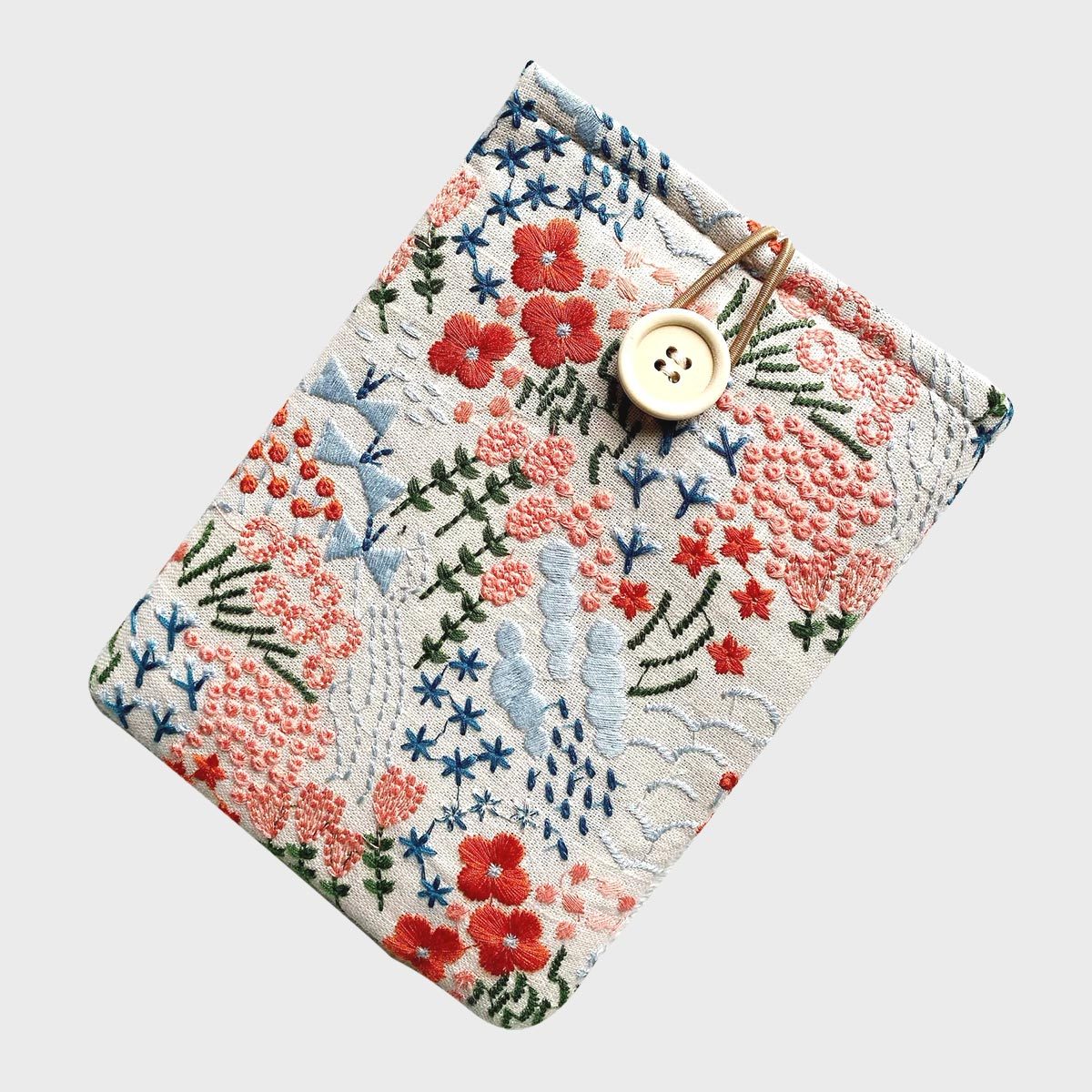 Cloth cover featuring embroidered flowers, shows assorted red, blue, and green patterns, with a button closure. Placed against a plain background.
