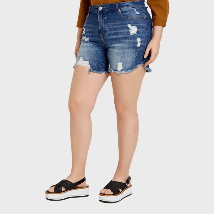 Denim shorts with frayed edges being worn. The setting is minimal, featuring a person standing. Sandals and casual attire complete the outfit.