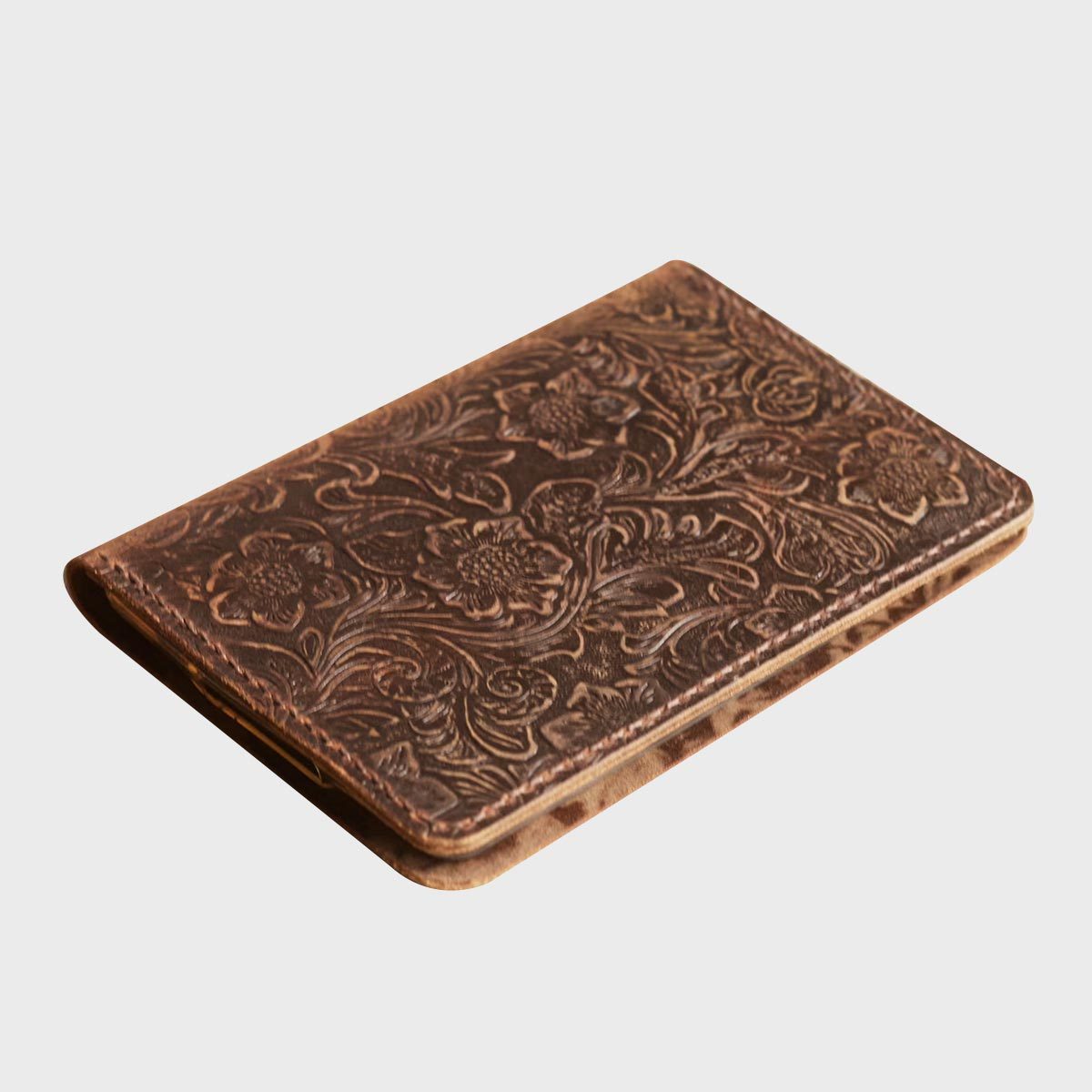 Leather wallet, resting, with embossed floral patterns on a plain gray background.