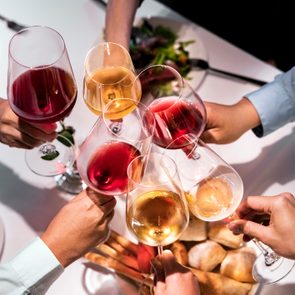 Hands clink wine glasses in a toast over a dining table with plates of food, including salad and bread.