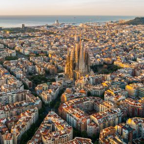 A grand cathedral stands centrally, surrounded by urban buildings, with the sea and horizon visible in the background, under a clear sky.