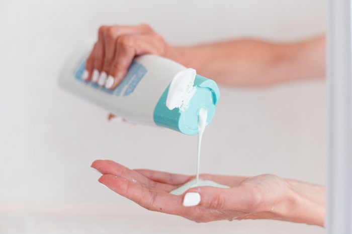 woman pouring body care lotion from bottle into her hand, closeup view, copyspace