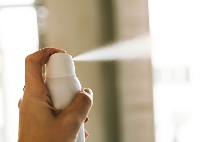 A bottle of white deodorant spray spraying a jet of air in a woman's hand