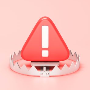 Red triangular warning sign rests inside an open bear trap, set against a soft pink background.