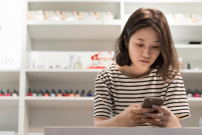 A young woman using smart phone in nail salon