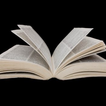 An open book has pages slightly lifted, resting against a black background.