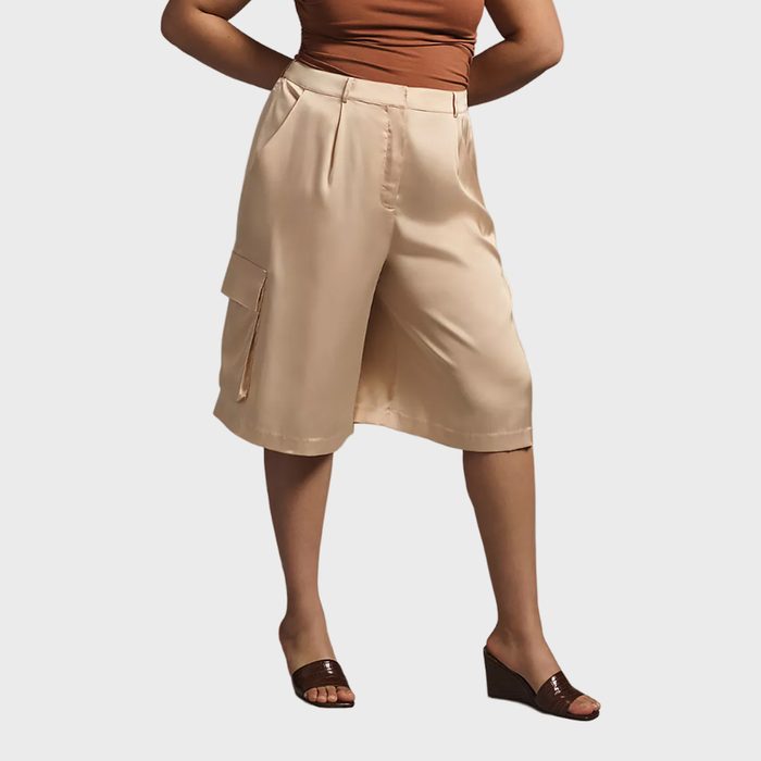 Beige knee-length shorts rest on a person's waist, paired with a brown top, set against a plain background.