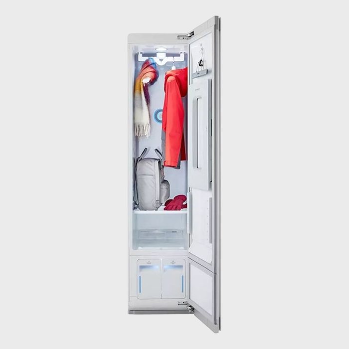 Wardrobe steams garments inside a narrow white cabinet, containing a red coat, multicolored scarf, and gloves, emphasizing clothing care technology in a home setting.