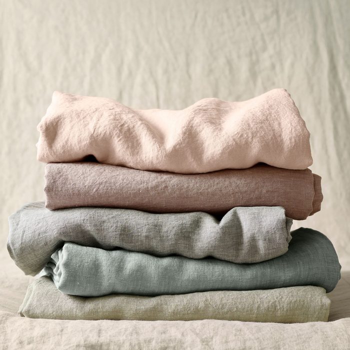 Four folded fabric pieces stacked, showing varying shades of beige and green; soft, textured appearance on a neutral background.