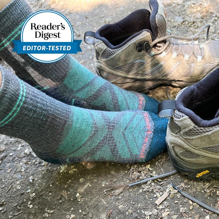 Socks cover feet beside hiking boots on a dirt path. A badge reads â€œReaderâ€™s Digest Editor-Tested.â€