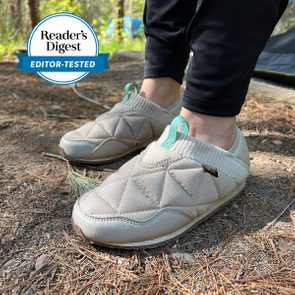Quilted slip-on shoes are worn on pine needle-covered ground, next to 