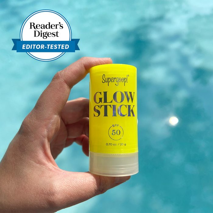 Hand holding a yellow Supergoop! Glow Stick SPF 50 by a bright blue pool, labeled 