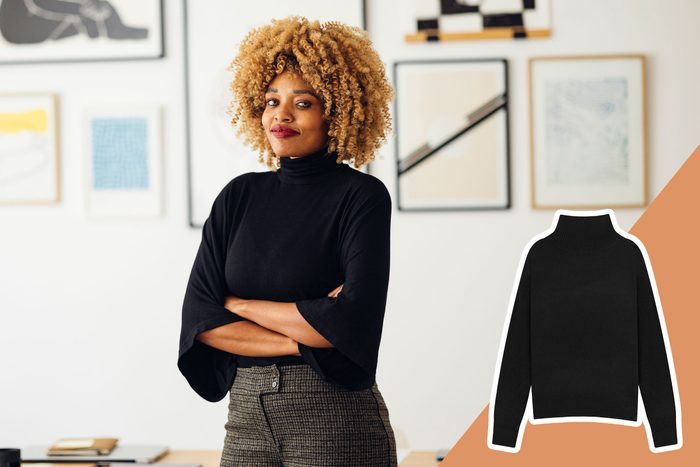 Person stands confidently with arms crossed; wearing black sweater, in an art-filled room. Inset shows sweater detail on an orange background.