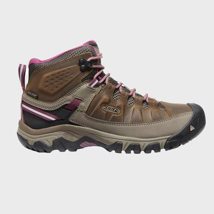 A rugged hiking boot sits against a plain gray background, featuring brown leather, pink accents, and thick, black treaded sole. Text reads 