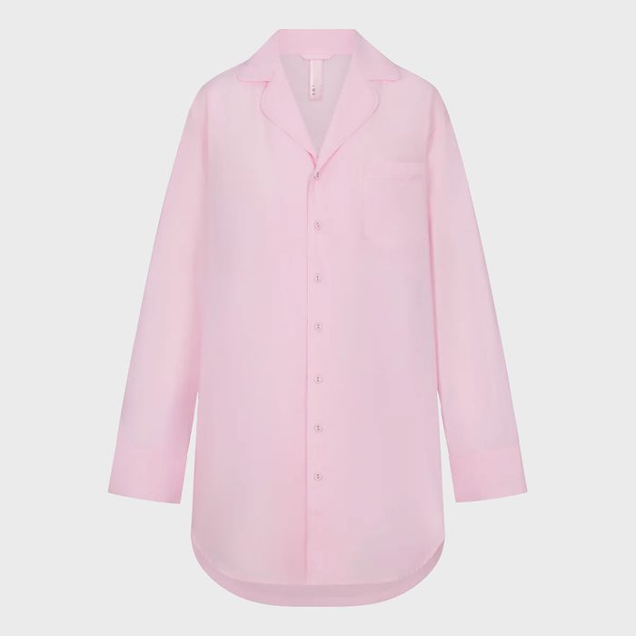 A pink button-up shirt hangs against a plain white background, featuring a pointed collar and a chest pocket.