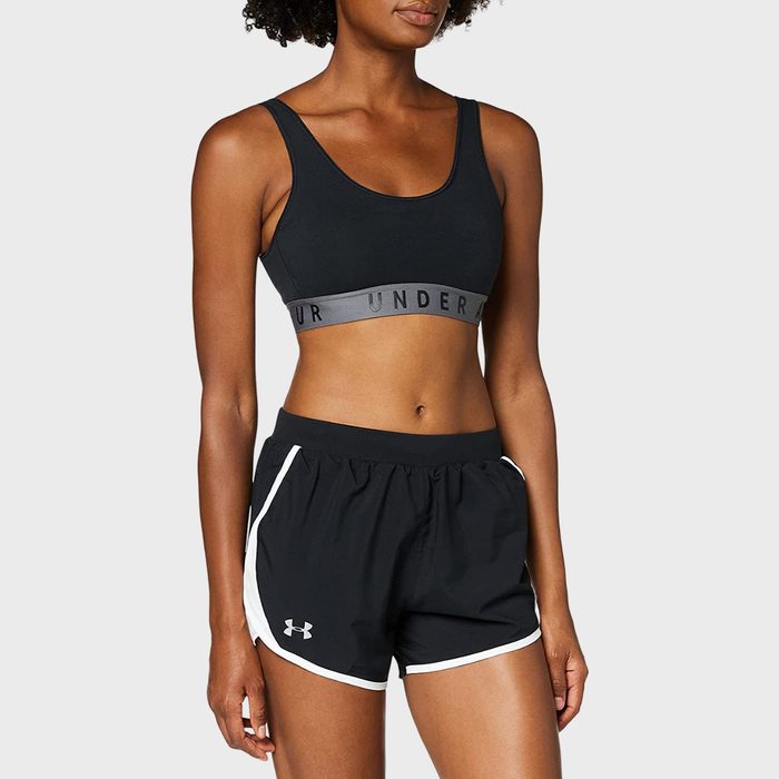 Person wearing black sports bra and shorts stands confidently against a plain gray background. 