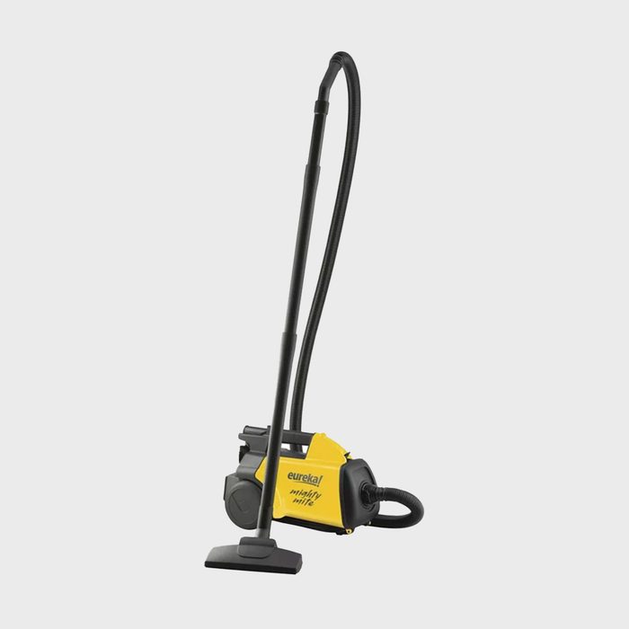Vacuum cleaner standing on floor, connected with hose and nozzle, against plain background. Text reads 