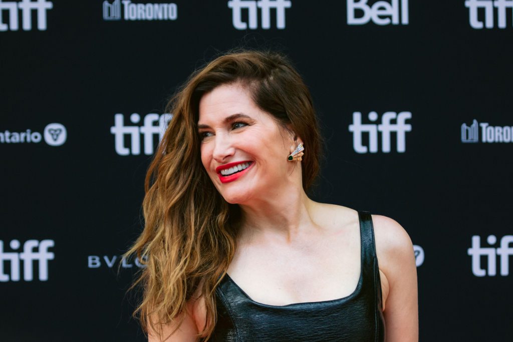 Person smiles, wearing a black outfit, on a TIFF event red carpet with logos "tiff," "Bell," "Ontario," "BVLGARI," "Toronto" in the background.