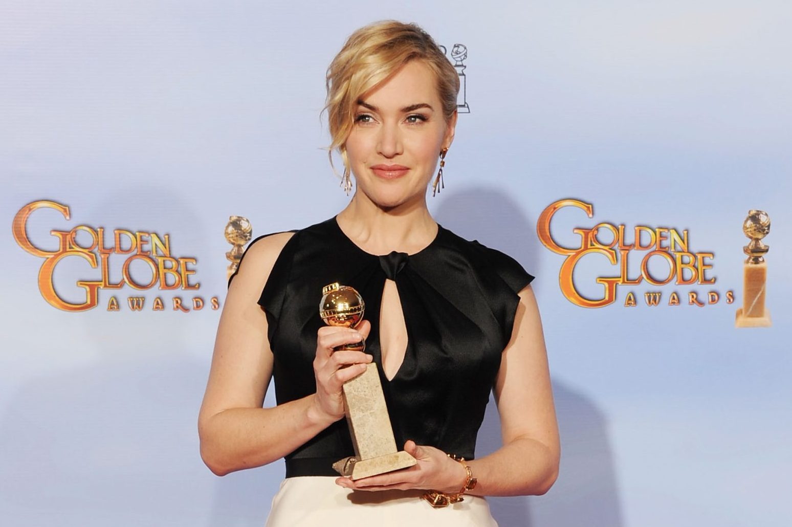 A person holding a Golden Globe trophy, smiling, stands in front of a backdrop with "Golden Globe Awards" logos.