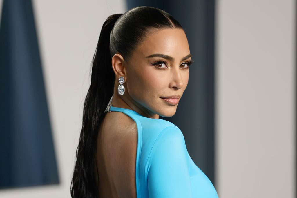 A person is looking over their shoulder, wearing a bright blue outfit with large earrings in a softly lit indoor setting.