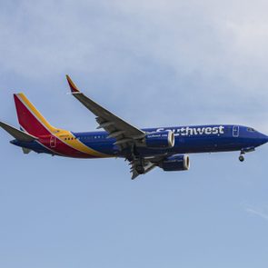 Airplane flies midair with landing gear down against a clear blue sky. Text reads, 