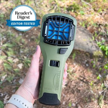 Device emits repellent, held by hand outdoors, surrounded by foliage; labeled "Thermacell MR300" with "Reader's Digest Editor-Tested" seal visible.