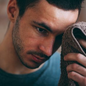 Person holding a towel to their face, appearing thoughtful, in a softly lit indoor setting.
