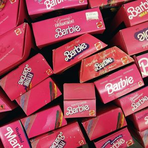 Barbie doll boxes, stacked haphazardly, feature bright pink packaging with various model names and the Mattel logo.