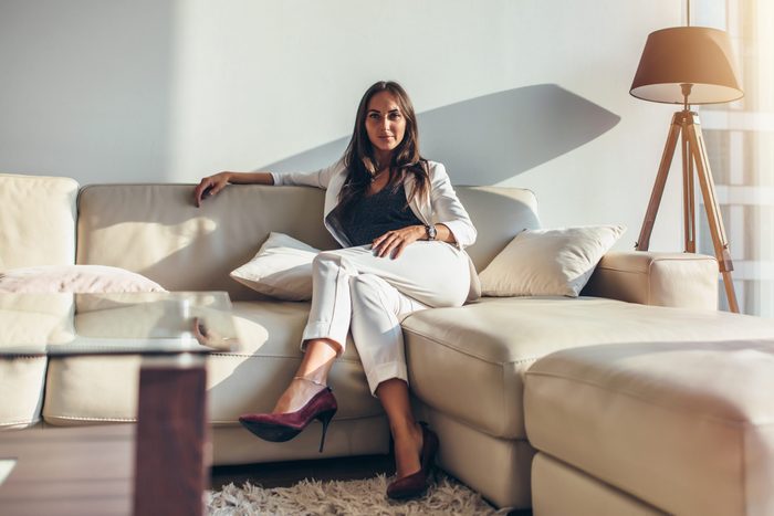Portrait of a woman sitting on sofa relaxing after work at home, dressed in the quiet luxury aesthetic