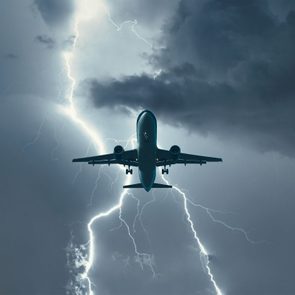 Airplane flies through dark stormy sky, illuminated by a bolt of lightning, surrounded by thick, ominous clouds.