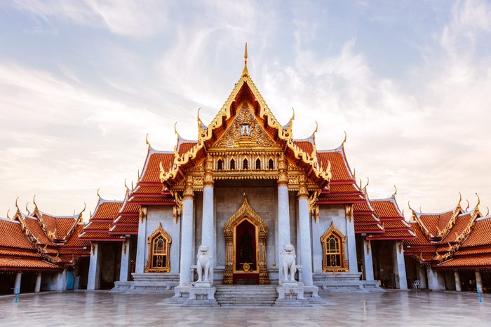 Temple stands with ornate golden roof, flanked by stone lion statues, set against a clear sky.