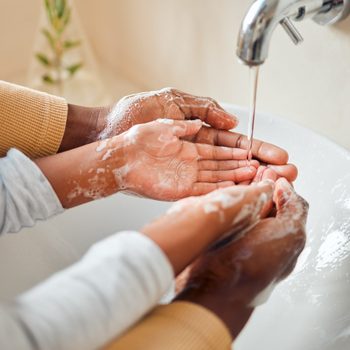 Hands wash with soap under running water in a white sink.