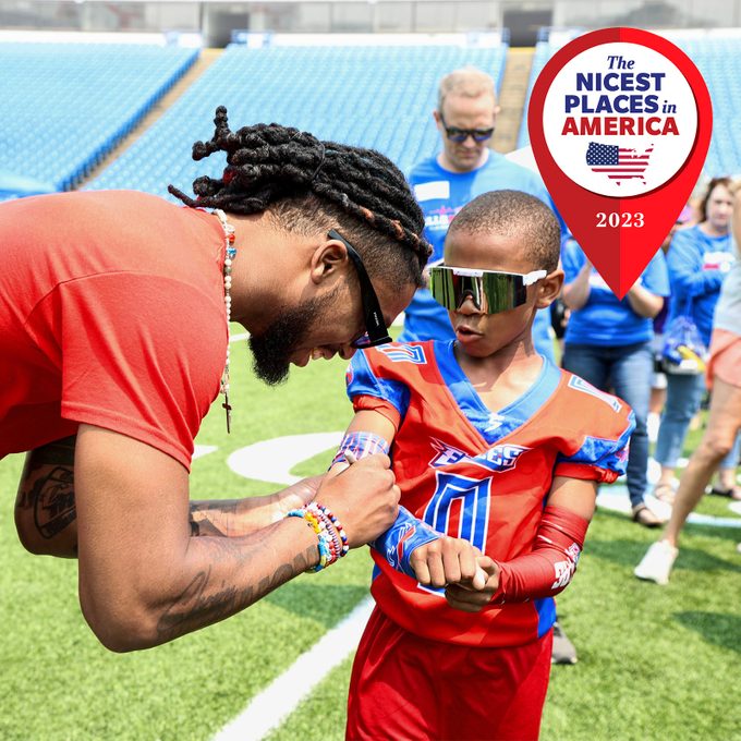 Man signs young football player's arm on field, surrounded by people. Sign reads 