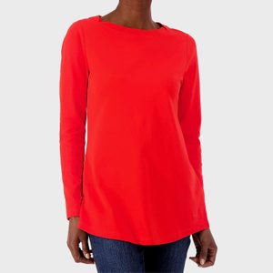 A person wears a vibrant red long-sleeve shirt, standing against a plain white background. The shirt is paired with dark blue jeans.