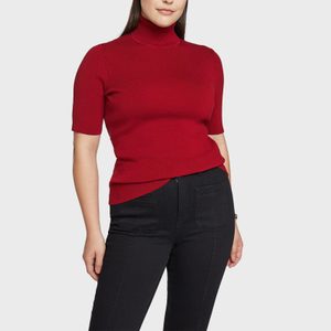 A person wearing a red turtleneck and black jeans stands against a plain white background.