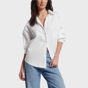 A person wears a white button-up shirt and blue jeans, standing casually against a plain light gray background.