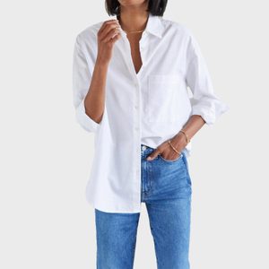 Person wearing a white button-up shirt with sleeves rolled slightly, paired with blue jeans, standing against a plain light gray background.