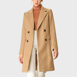 A tan double-breasted coat drapes over a person wearing a brown turtleneck and white pants, against a plain background.