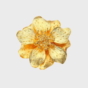 Gold flower brooch resting against a plain white background, showcasing intricate petal textures and central clustered decorations.