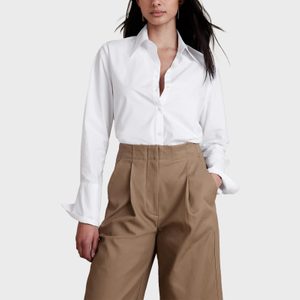 Person wearing a white button-down shirt and beige trousers stands confidently against a plain, neutral background.