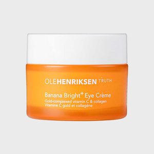 Orange jar holds Banana Bright+ Eye CrÃ¨me, featuring gold-complexed vitamin C. White lid contrasts jar in minimalist setting. Text: OLEHENRIKSEN TRUTH.