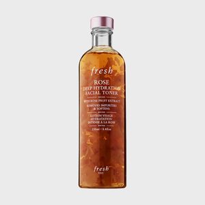 A clear bottle contains rose facial toner with floating petals, labeled 