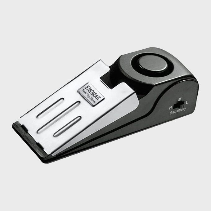 Doorstop alarm sits on a flat surface; silver and black with sensitivity settings, labeled 
