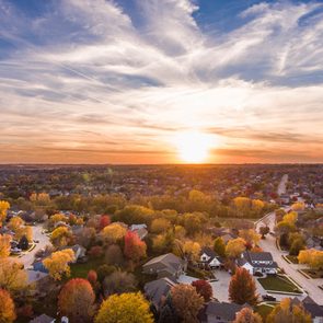 Sunset illuminates suburban neighborhood with winding roads and autumn trees, creating a colorful landscape under a dramatic sky full of clouds.
