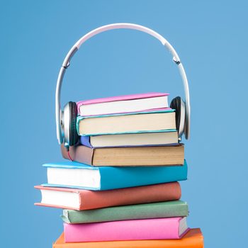 Books stacked with headphones placed on top, against a solid blue background.