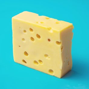 A block of Swiss cheese stands upright on a bright blue surface, showcasing its distinctive holes.