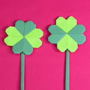 Two origami clovers stand against a bright pink background.