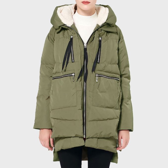 Green puffer coat with a hood is worn by a person, featuring zippers and black drawstrings; background is plain light gray.