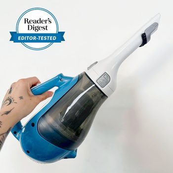 Hand holds a small blue and white handheld vacuum, angled downwards, against a plain white background. Text says "Reader's Digest Editor-Tested."